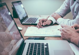 people in meeting on laptops with pens and paper desk